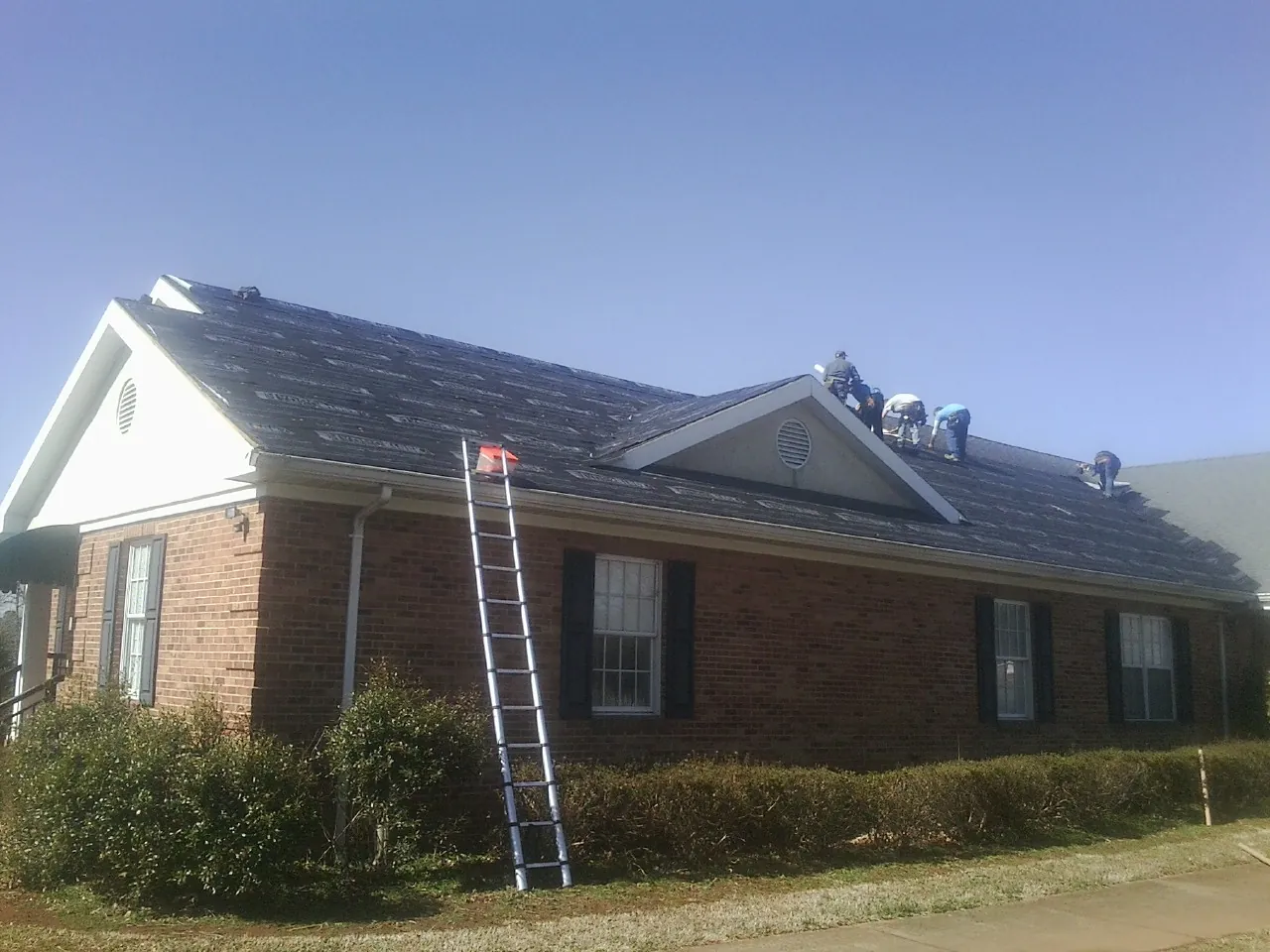 Crew tearing shingles off a brick ranch roof with a ladder set — Emergency Roof Repair work by our crew in Budd Lake