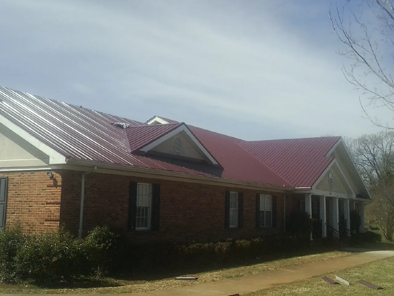 Red metal roof with gabled entries on a long brick building, from a Hail Damage Roof Repair job in Budd Lake