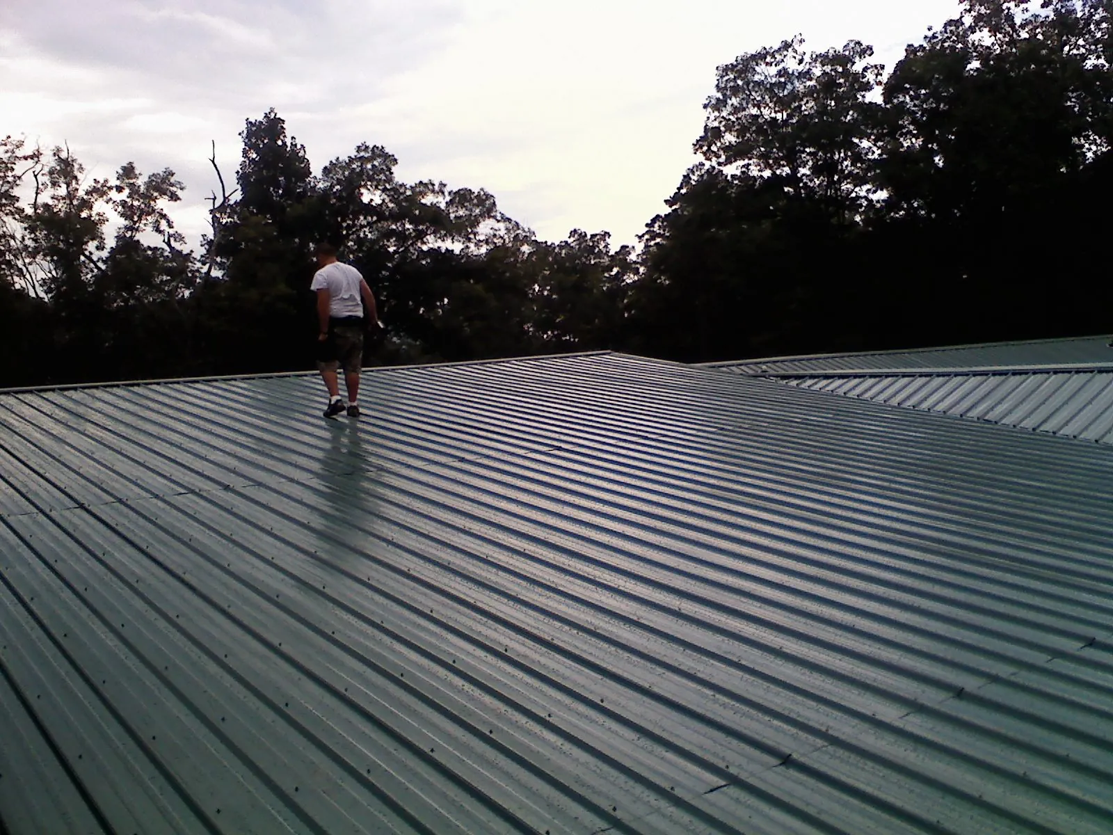 Roofer walking a wide expanse of new green metal roofing in Budd Lake