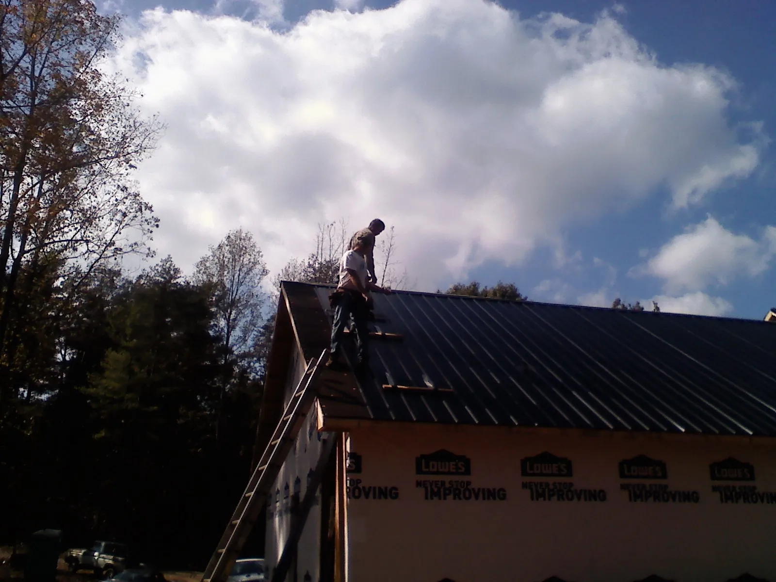 Roofer fastening dark metal panels high against a cloudy sky, from a Roof Inspection job in Budd Lake