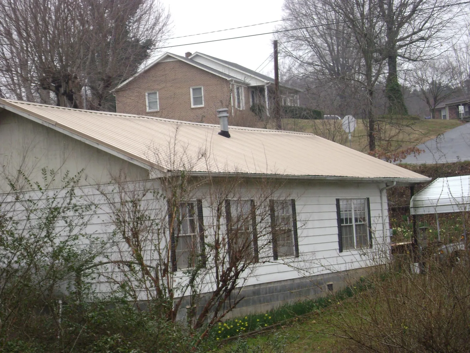 Tan metal roof on a white sided house set into a hillside — Commercial Roofing by Roofing Brothers in Budd Lake